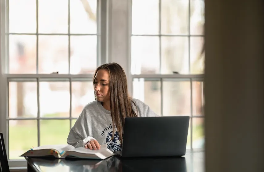 student at laptop, glancing aside at notes